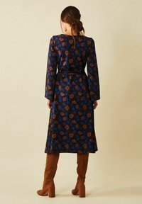 Långärmad klänning i blått med brunt blommönster, med bälte i midjan. Matchad med bruna klackstövlar. Slät textur.