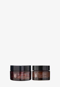 Dwa bursztynowe słoiki z czarnymi zakrętkami oznaczone jako True Botanicals Phyto-Retinol Vitamin A Booster i Sleep Mask na białym tle.