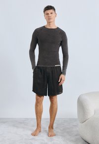 Tričko s dlhým rukávom v tmavosivej farbe s okrúhlym výstrihom, kombinované s čiernymi krátkymi nohavicami. Ležérny strih, mäkká textúra, so zvýraznenými švami a detailmi na páse.
