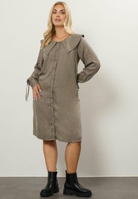 Rutig klänning i brunt och krämfärgat, med en stor krage, knäppning framtill och långa ärmar med band. Bärs med svarta ankelkängor.