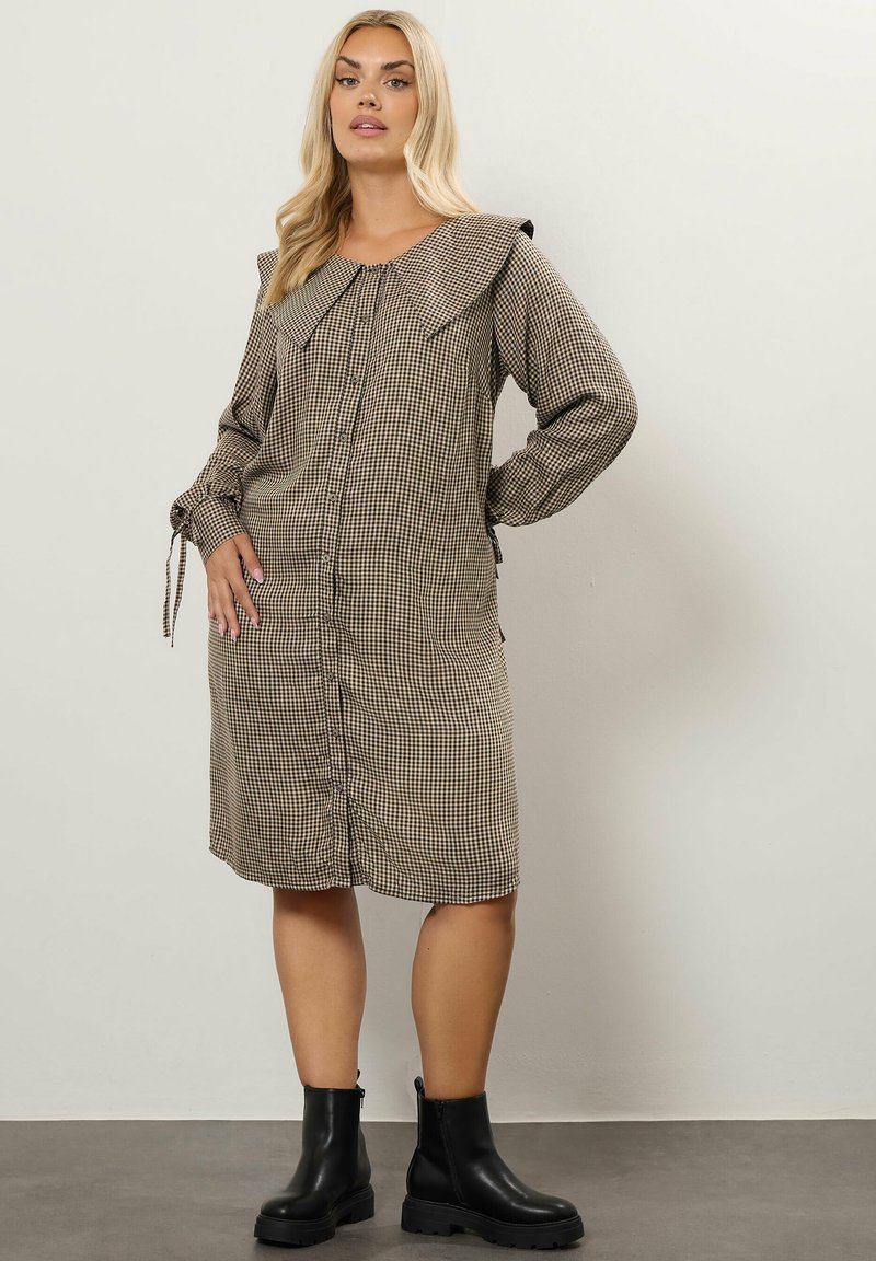 Rutig klänning i brunt och krämfärgat, med en stor krage, knäppning framtill och långa ärmar med band. Bärs med svarta ankelkängor.