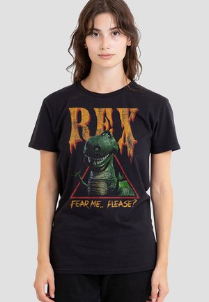 Young woman wearing black T-shirt with smiling green T-Rex inside red triangle and text "REX" and "FEAR ME.. PLEASE?" on gray background.