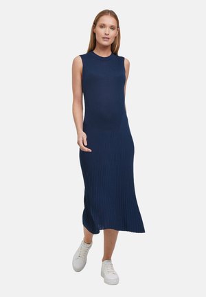 Navy ribbelgebreid jurk met een mouwloze uitvoering, een ronde hals en een middellange zoom, gecombineerd met witte sneakers. Soepele textuur.