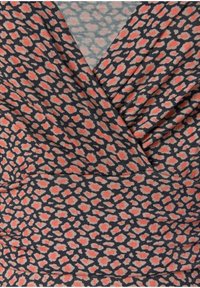 Mönstrad topp med en mörk marinblå bakgrund och korallfärgade samt beige prickar. Den har en crossover-design med gathered tygdetaljer.