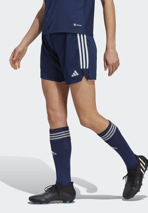 Marineblauwe sportshorts met witte zijstrepen, gemaakt van ademende stof. Gecombineerd met kniehoge marineblauwe sokken met witte strepen en zwarte voetbalschoenen.