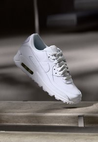 Weiße Sneakers mit sichtbarem Luftpolster schweben über steinernen Stufen im sanften natürlichen Licht.