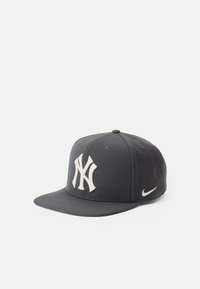 Sivá baseballová čiapka s plochým okrajom, na ktorej sa nachádza veľké biele vyšívané logo New York Yankees a malé biele logo Nike swoosh na boku.