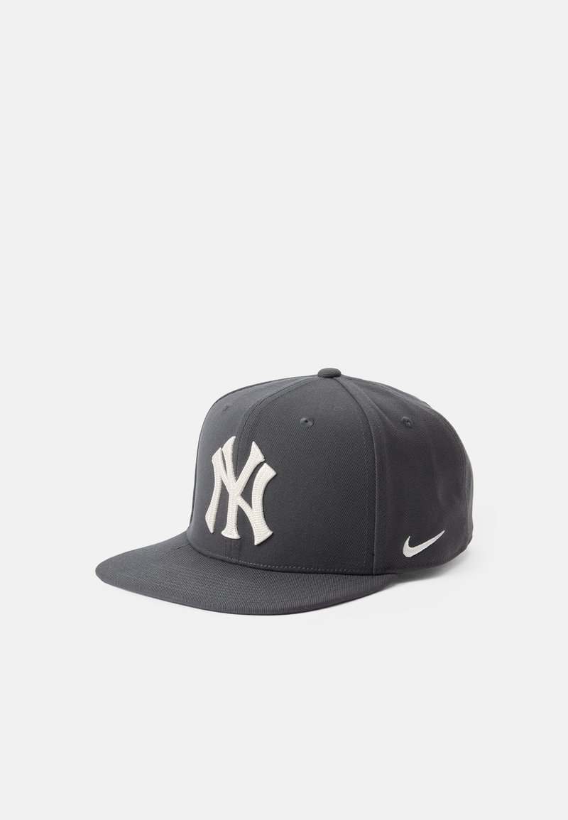 Sivá baseballová čiapka s plochým okrajom, na ktorej sa nachádza veľké biele vyšívané logo New York Yankees a malé biele logo Nike swoosh na boku.