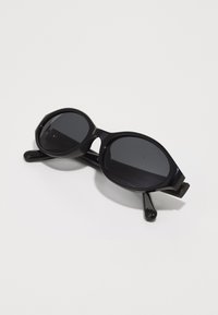 Lunettes de soleil noires avec une finition brillante, verres ovales, design de monture proéminent et branches courbées. Détails notables comprenant un logo subtil sur la branche.