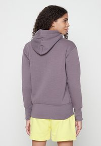 Lila Kapuzenpullover mit lockerer Passform, gerippten Bündchen und Saum. Getragen mit gelben Shorts, die einen lässigen Stil betonen.