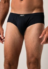 Černé pánské slipy vyrobené z hladkého materiálu, s jednobarevným vzhledem a elastickým páskem s logem. Střih je těsný s nízkým pasem.