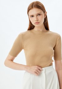 Beige geribbelde T-shirt met korte mouwen, voorzien van een aansluitend ontwerp en een ronde hals. De stof heeft een zachte textuur en is gecombineerd met hoge witte broeken.