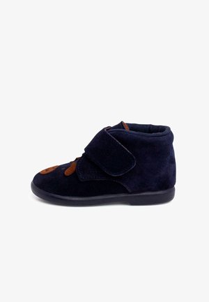 Bota de ante azul oscuro con acentos marrones y una correa de velcro. Forma de punta redonda, cuello acolchado y suela flexible de goma negra.
