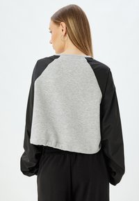Geknipte sweatshirt met een grijze fleece lijf en zwarte nylon mouwen. Heeft een ronde halslijn en een elastische zoom. Minimalistisch ontwerp.