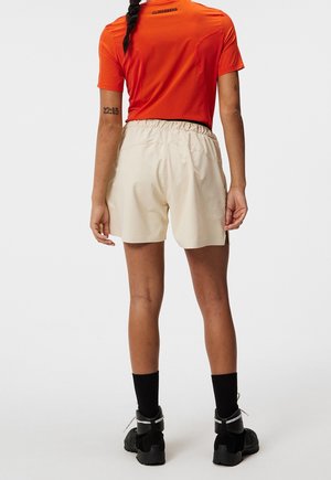 Beige korte broek met een elastische tailleband, gecombineerd met een oranje T-shirt met korte mouwen. Zwarte sokken en stevige zwarte schoenen maken de outfit compleet.
