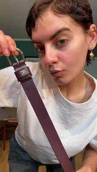 Lila bőr öv arany csattal és texturált pánttal. Kör alakú díszítéssel, rajta bemélyesztett logóval.