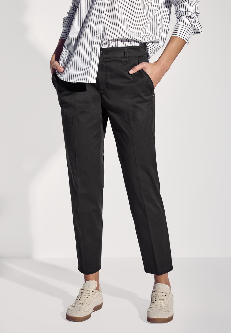 Zwarte cropped broeken met een rechte snit, zijzakken en een gladde textuur. Gecombineerd met crèmekleurige sneakers met een gestructureerd oppervlak.