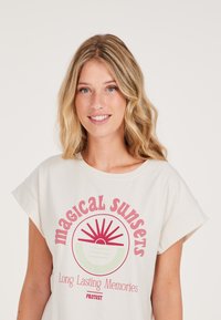 Kreminės spalvos marškinėliai su suvirintomis rankovėmis, kuriuose yra grafikos atspaudas su saule ir tekstu "Magical Sunsets" rožiniais ir žaliais atspalviais.