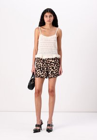 Top en dentelle crème avec un ourlet à volants porté sur un short imprimé léopard noir et beige. Sac à main noir et sandales à talons noires à lanières complètent la tenue.