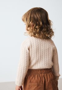 Beige stickad tröja med ribbade och flätade mönster, kombinerad med rostfärgade manchesterbyxor med elastisk midja och två fickor.