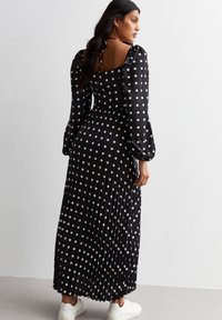 Black, long-sleeve dress with a square back and tie detail, featuring white polka dots and a pleated skirt. Worn with white sneakers.