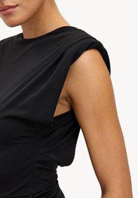 Robe noire sans manches avec détails plissés sur l'épaule, texture lisse, coupe ajustée et conception latérale ouverte pour la ventilation.