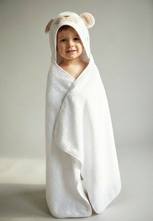 Young child wrapped in white towel with animal face hood, standing against plain light gray background.