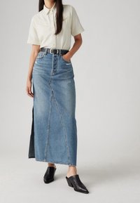 Ljust beige kortärmad skjorta, högmidjad blå denimmaxikjol med sidoklyfta, i kombination med svarta klackmuller.