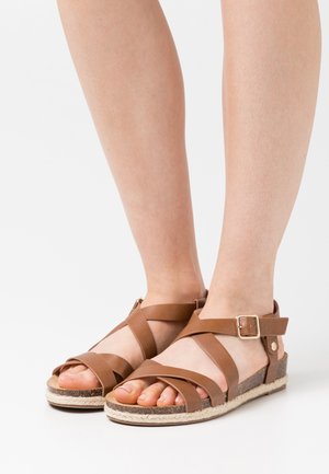 Sandales brunes à lanières avec une boucle de cheville, présentant une semelle en toile tissée de style espadrille et des lanières en cuir lisse.