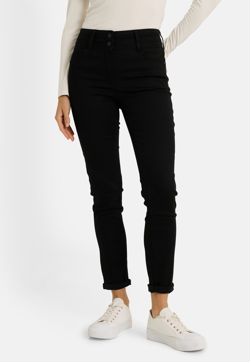 Jean noir taille haute coupe slim, avec deux boutons devant, revers roulés, en tissu mélange coton. Porté avec des baskets blanches.