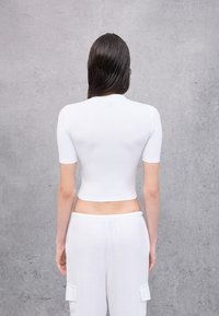 Weißes, kurzärmeliges Cropped-T-Shirt aus glattem Material, kombiniert mit locker sitzenden, hellen Hosen.