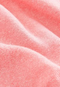 Gros plan d'un tissu rose doux avec une fine texture tissée en diagonale et des plis doux créant des variations de lumière et d'ombre.