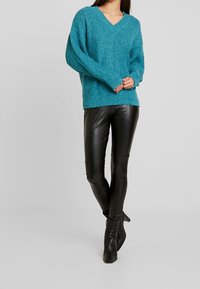 Tealstickad tröja med v-ringning, ribbad textur och fallande axlar, ihopparad med svarta åtsittande läderbyxor och svarta klackboots.