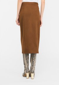 Gonna midi in suede marrone con un design aderente e cuciture a vista, abbinata a stivali in tinta unita con stampa pitone al ginocchio e tacco a blocco.