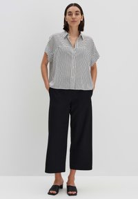 Blusa a righe bianco e nera con maniche corte, chiusura a bottoni e vestibilità ampia, abbinata a pantaloni larghi neri a vita alta.