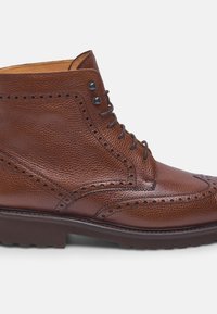 Stivale alla caviglia in pelle marrone con dettagli brogue, cinque occhielli e una finitura testurizzata con suola in gomma per una migliore trazione.