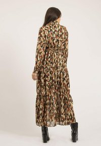 Robe longue à volants avec un motif de feuilles, présentant des teintes dorées, rouges, crème et noires. Fabriquée en tissu transparent, avec des manches ajustées et une ceinture.
