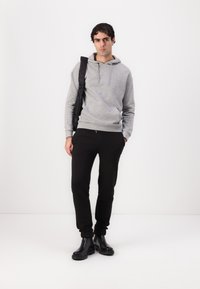 Sweatshirt gris à capuche avec une poche kangourou, associé à un pantalon de jogging noir et des bottines noires brillantes, le tout porté avec un sac noir à l'épaule.