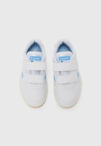 Baskets blanches avec des accents bleus, deux bandes Velcro, et une zone des orteils perforée. Comprend une semelle en caoutchouc et un logo Lacoste sur la languette.