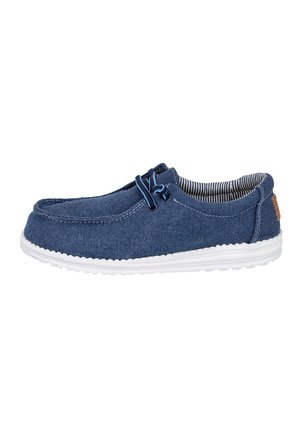Zapato casual de lona azul tipo slip-on con suela blanca, cordones elásticos azules y forro interior a rayas, mostrado de lado.