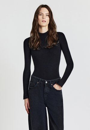 Top nero a costine a maniche lunghe con colletto alto, abbinato a jeans in denim scuro a gamba larga con tasche frontali e chiusura con bottone.