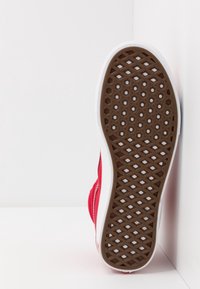 Baskets rouges avec une semelle en caoutchouc texturé marron, une semelle intermédiaire blanche et un dessus en tissu lisse. Présente un design bas et sans logos visibles.