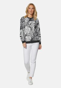 Zwarte sweatshirt met een witte tropische bladenprint, ronde halslijn en geribde manchetten. Gecombineerd met witte slim-fit jeans en witte sneakers.