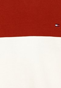 Maglione a blocchi di colore rosso e bianco realizzato in morbido tessuto a maglia. Presenta un piccolo logo nell'angolo. Texture liscia con una vestibilità classica.