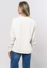 Vit sweatshirts med rund halsringning och långa ärmar, med en avslappnad passform och mjuk textur. Matchas med blå jeans.