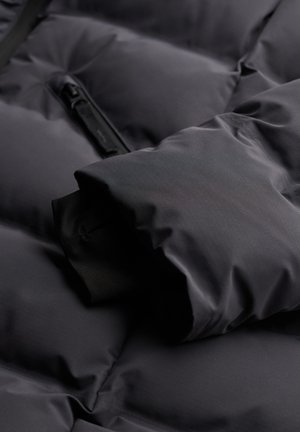 Czarna kurtka puchowa w zbliżeniu, z pikowanym wzorem, miękkim materiałem i detalem zamka błyskawicznego. Manżetka ukazuje gładką podszewkę.