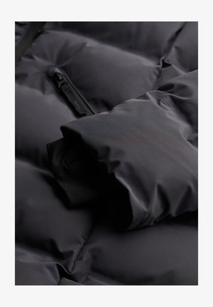 Schwarze Daunenjacke Nahaufnahme, mit gesteppter Textur, weichem Material und einem Reißverschluss-Detail. Der Bund zeigt eine glatte Innenauskleidung.