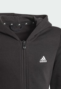 Felpa con zip nera con cappuccio e logo Adidas bianco. Realizzata in materiale morbido con una superficie liscia e chiusura a zip frontale.