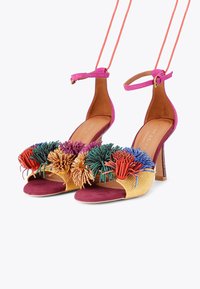 Sandali con tacco alto con un cinturino alla caviglia rosa, materiali dorati e bordeaux, caratterizzati da un design vivace con pompon di diverse texture e tonalità.