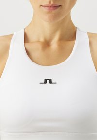 Λευκό αθλητικό κοντομάνικο μπλουζάκι από λεία ύφανση με μαύρο λογότυπο κεντραρισμένο στο στήθος, στρογγυλή λαιμόκοψη και φαρδιές χελιδονοουρές.